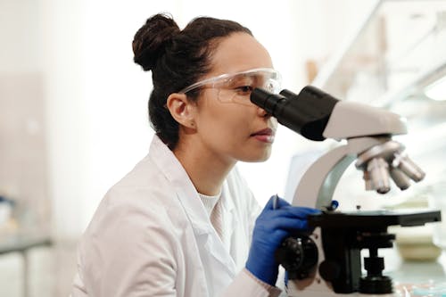 Free Female Scientist in White Lab Coat Using a Microscope Stock Photo