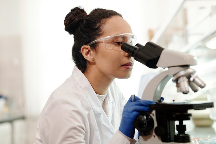 Female Scientist In White Lab Coat Using A Microscope