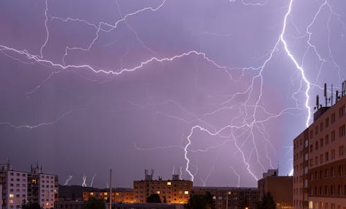 Powerful bright lightning strike in purple sky over modern city district in evening