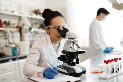 Free Female Scientist in White Lab Coat Using a Microscope Stock Photo
