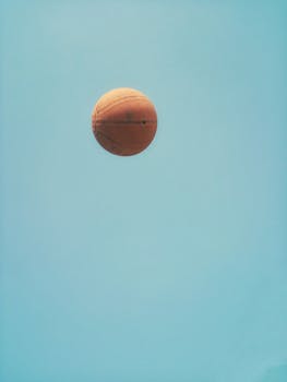 A basketball captured mid-air against a pristine blue sky with ample copy space.