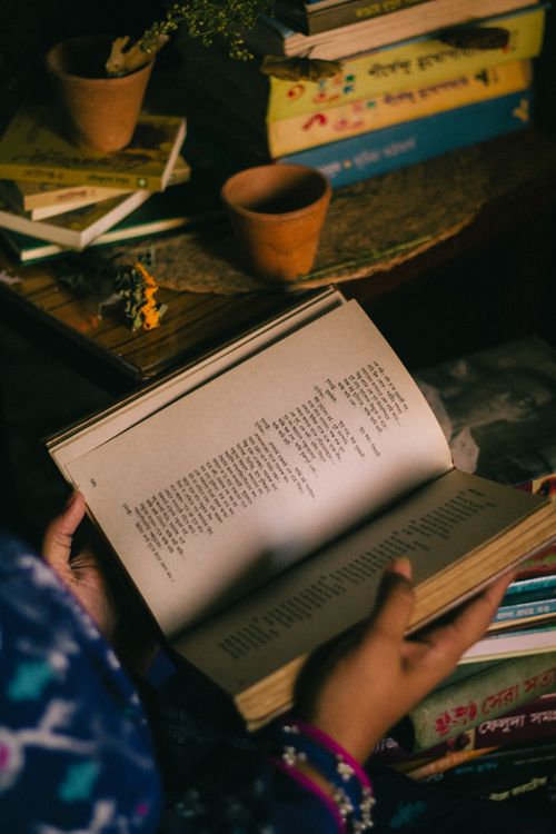 Free A person reading a Bangla book indoors, surrounded by more books and warm lighting. Stock Photo