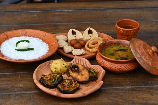 Authentic Bengali cuisine with rice, fried fish, and sweets served in clay pottery.