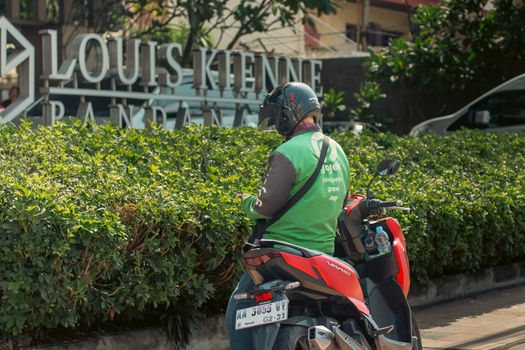 Delivery rider on motorcycle waiting outside Louis Kienne Pandanaran hotel entrance.