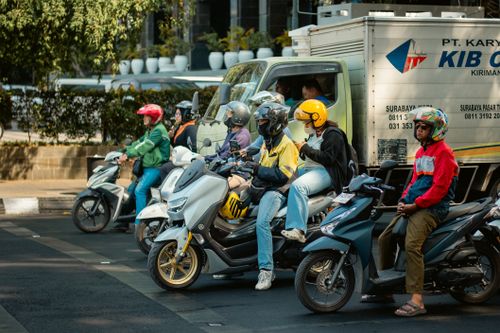 Free Motorcyclists waiting at a city traffic light alongside a truck on a sunny day. Stock Photo