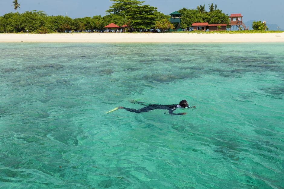 A snorkeler glides through crystal-clear waters near a tropical beach in Semporna, Sabah, Malaysia.