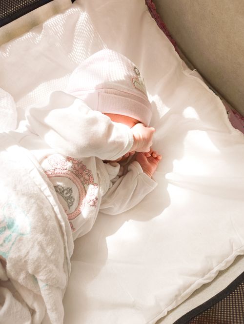 Free A newborn baby resting peacefully on a white blanket with gentle sunlight streaming in. Stock Photo