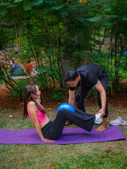 Free Woman exercising with a trainer outdoors on a yoga mat with a fitness ball. Stock Photo