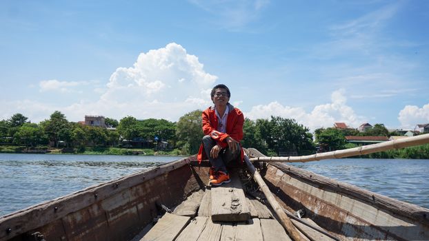A young man smiles while sitting in a boat on a sunny day in Hue, Vietnam.