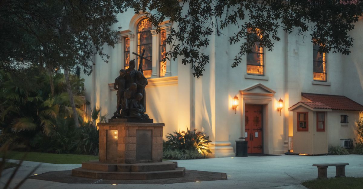 Beautiful night view of a historic statue beside a lit building in St. Augustine, Florida.