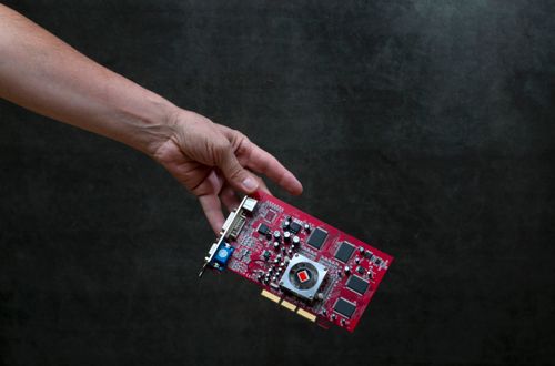 Free A close-up of a hand holding a red graphics card against a dark textured background. Stock Photo
