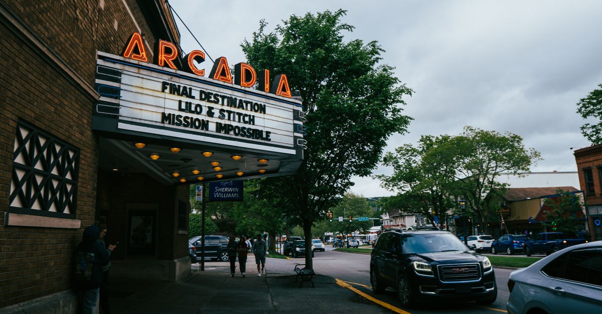Street view of Arcadia cinema with neon sign displaying movie titles in a lively urban setting.
