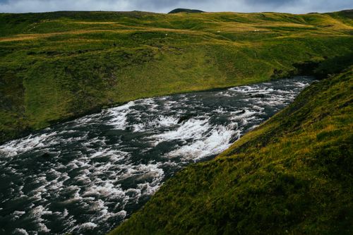 Free Vibrant river flowing through lush green hills in Rangárþing eystra, Iceland's picturesque landscape. Stock Photo