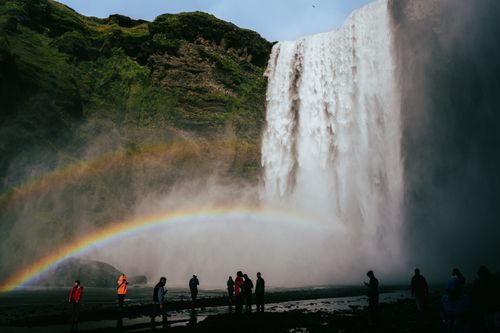 Free Beautiful view of Skógafoss waterfall in Iceland with a bright rainbow and visitors below. Stock Photo