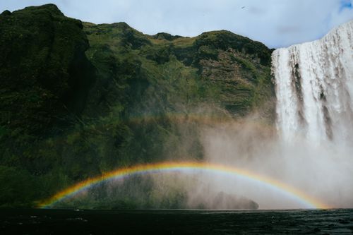 Free Capture of Skógafoss waterfall in Iceland with a vibrant rainbow arching through the mist. Stock Photo
