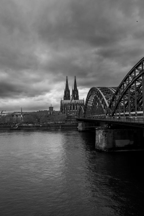 Free Black and white view of Cologne Cathedral and Hohenzollern Bridge over the Rhine River, under dramatic clouds. Stock Photo