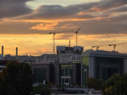 Free A cityscape at sunset featuring construction cranes and office buildings under a dramatic sky. Stock Photo