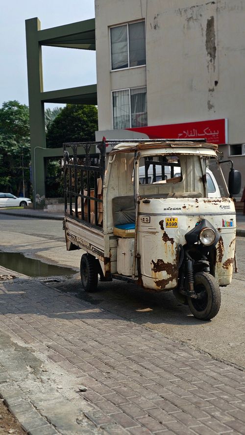 Free A worn tuk-tuk parked on a sunny street in Lahore, capturing local urban life. Stock Photo