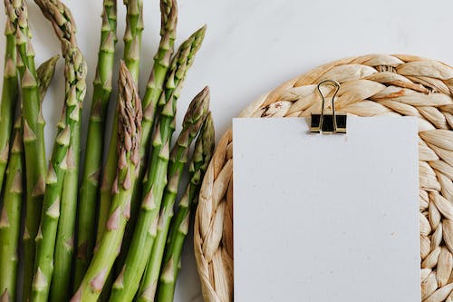 Free Top view of asparagus pods with sheets of paper fastened by paper clip on white desktop Stock Photo