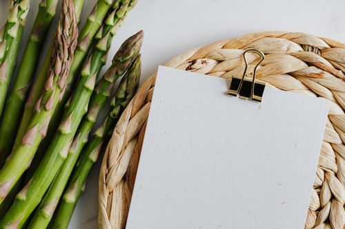 Free Asparagus stalks beside a blank notepad on a woven mat, ideal for food and note-taking concepts. Stock Photo