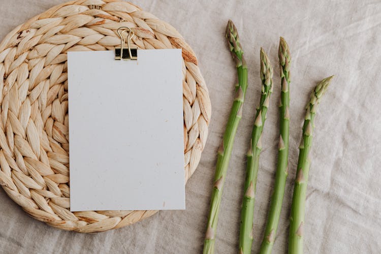 Asparagus Sprouts And Blank Paper Over Wicker Placemat On White Tablecloth