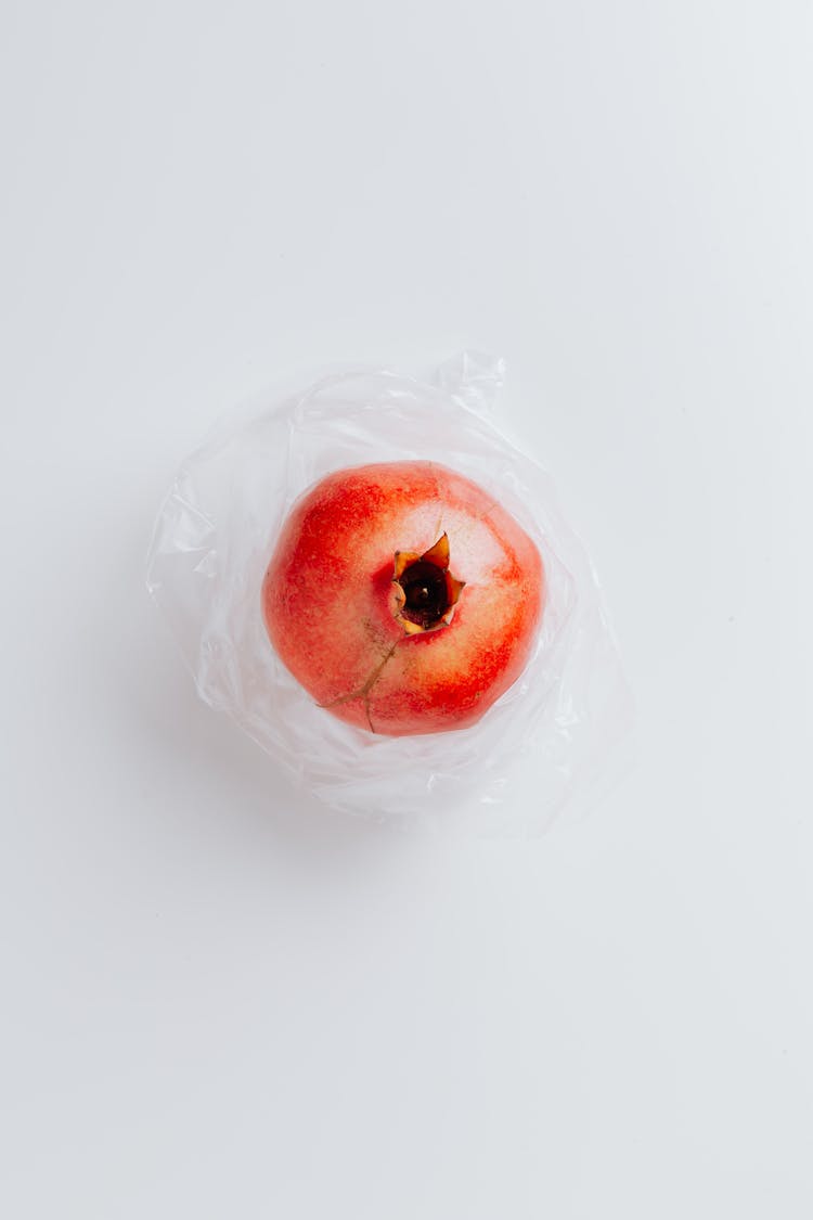 Ripe Pomegranate On Polyethylene Bag On Gray Background