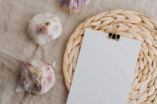 Free Flat lay of garlic bulbs with a blank card on a woven placemat with earthy tones. Stock Photo