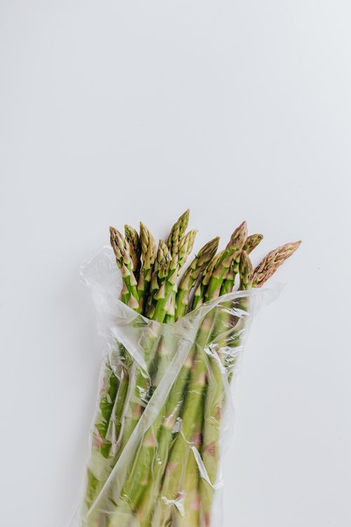 Free Bundle of thin green fresh asparagus with dense stalks and soft elastic ends put in transparent plastic bag on white background Stock Photo