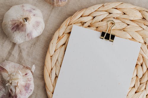 Sheet of white empty paper fixed with clip near garlic