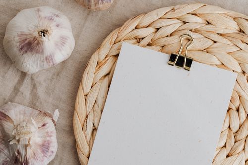 Free From above of blank paper wit metal clip placed on wicker table mat near raw heads of garlic Stock Photo