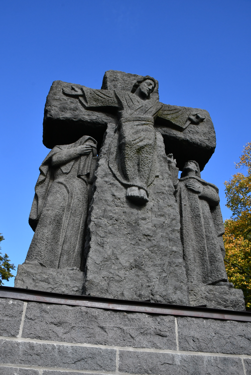 Free A stone crucifix monument with figures under a clear blue sky, highlighting religious artistry. Stock Photo