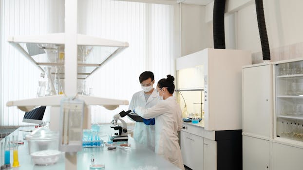 Two scientists wearing protective gear collaborating in a laboratory setting with modern equipment.