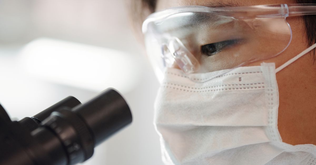 Close-up of a scientist wearing safety gear using a microscope indoors.