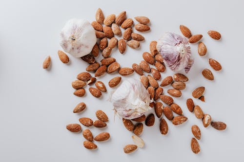 Raw almonds and heads of garlic on white background