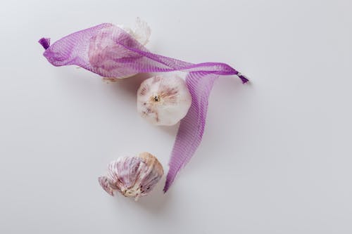 Composition of garlic bulbs with purple net on white background