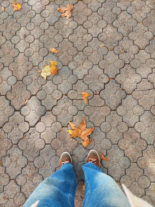 Free Feet in jeans on a patterned sidewalk with scattered autumn leaves. Stock Photo