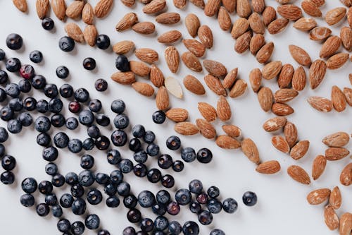 Raw almonds and fresh blueberries put on white surface