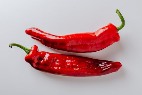From above of pair of hot chili peppers with green sprouts and smooth surface put on white table