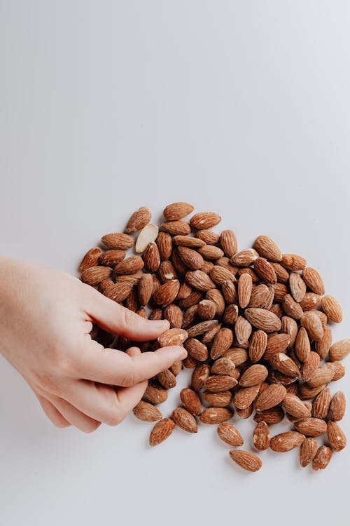 Crop person taking almond nut from white table