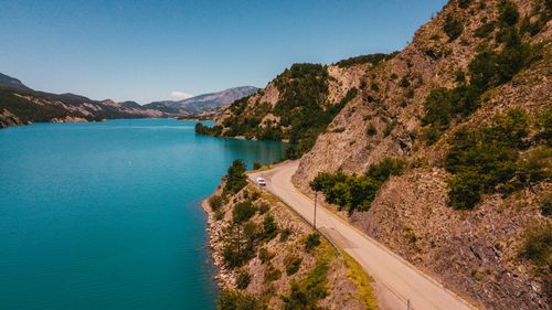Free A breathtaking aerial view of a winding road along a turquoise mountain lake under a clear blue sky. Stock Photo