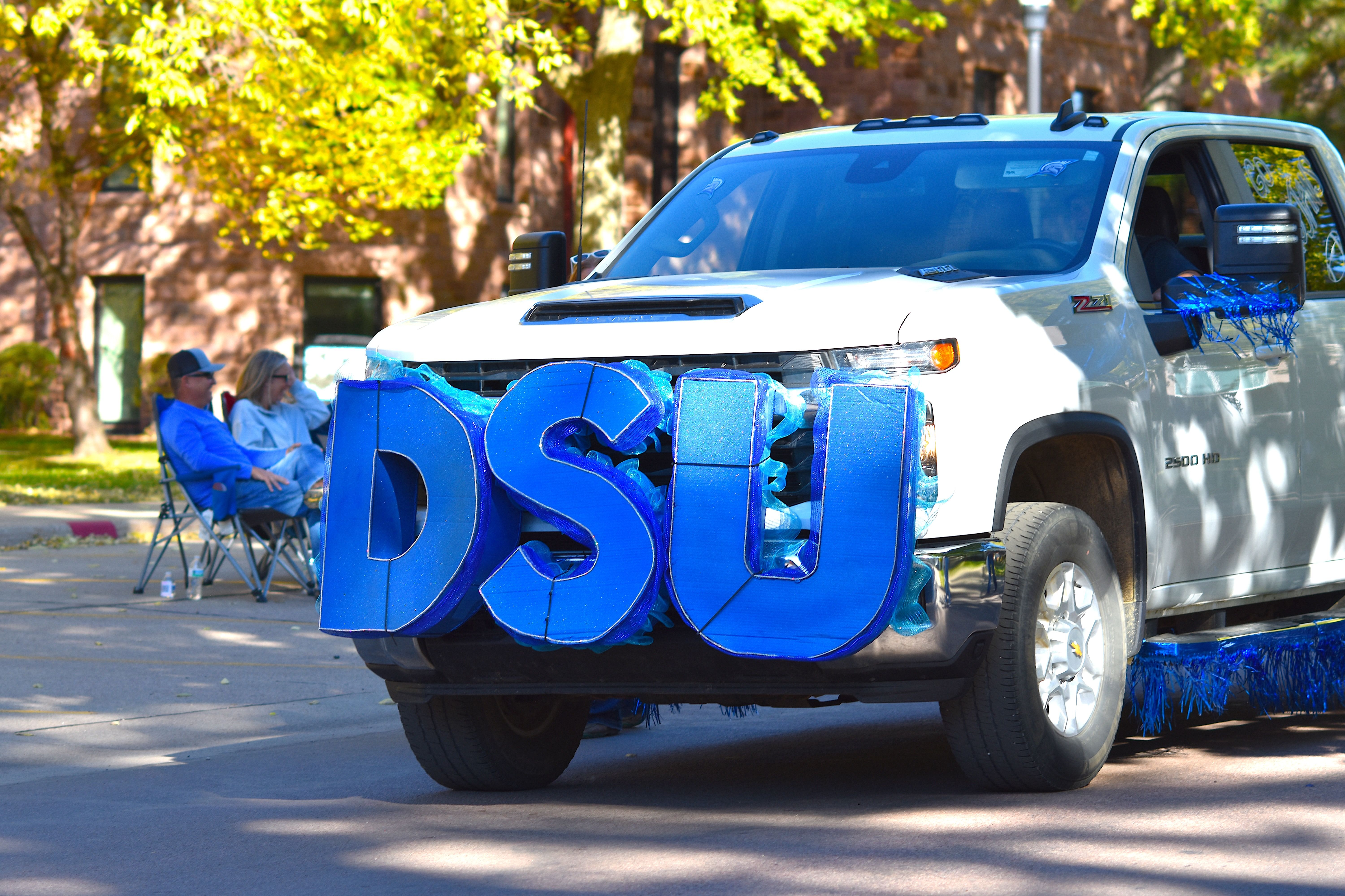 White pickup truck decorated with large blue DSU letters for a parade event in autumn setting.