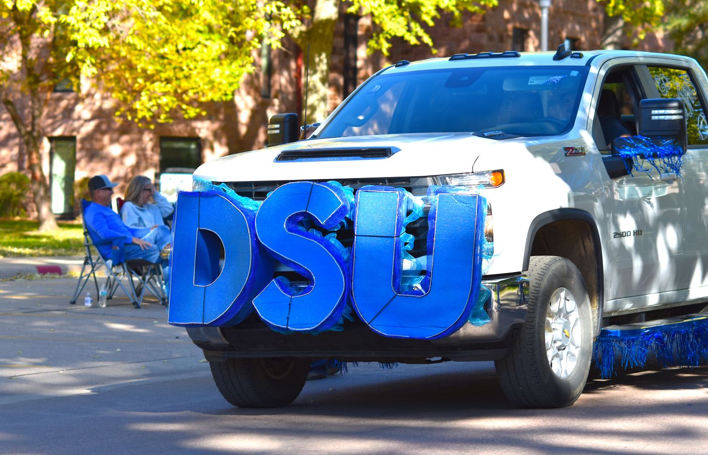 White pickup truck decorated with large blue DSU letters for a parade event in autumn setting.