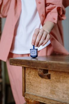 Close-up of a person in pink attire spinning a blue dreidel on a rustic table.
