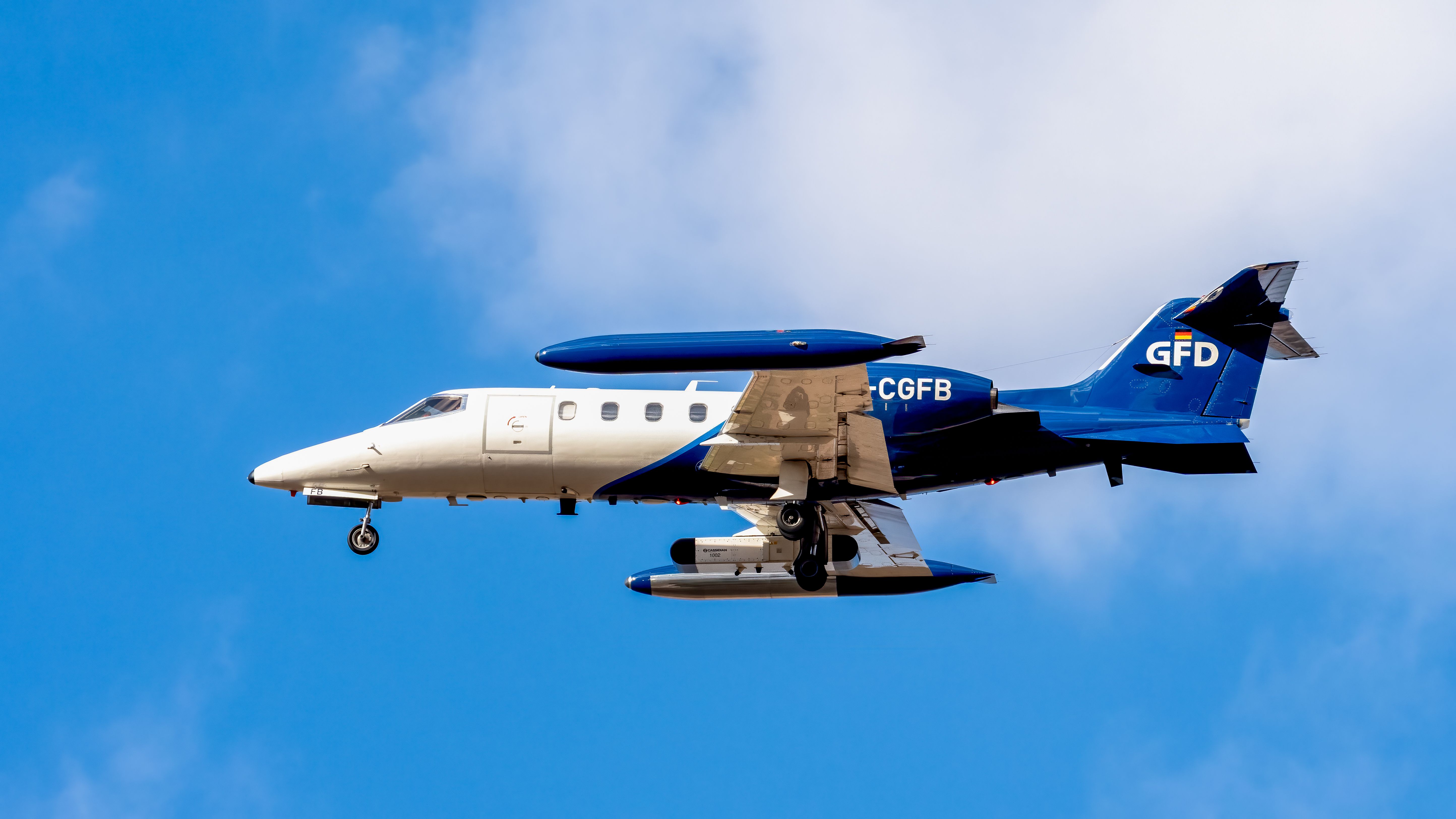 High-angle view of a military aircraft mid-flight against a blue sky with clouds.