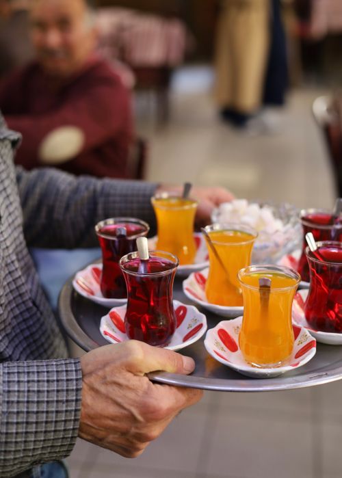 Free A waiter holding a tray with traditional Turkish tea and orange juice in a vibrant cafe setting. Stock Photo