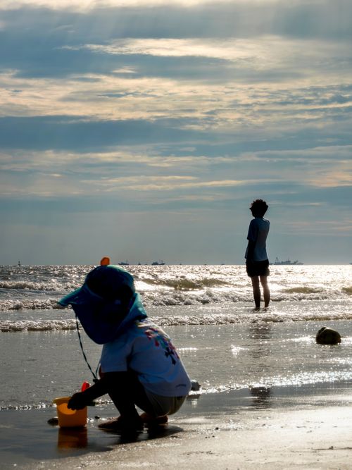 Free A child plays with a bucket on the beach while an adult gazes at the sea in Beihai, China. Stock Photo
