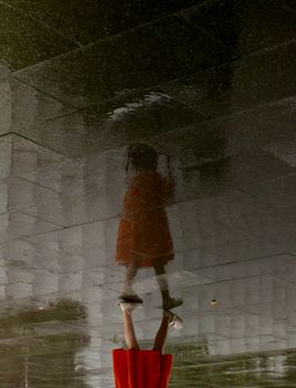 Artistic reflection of a child in a puddle on a rainy day in Guangzhou, China.