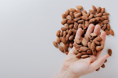 Free From above of anonymous male taking tasty organic almonds from pile of nuts placed on white background isolated illustrating healthy food concept Stock Photo