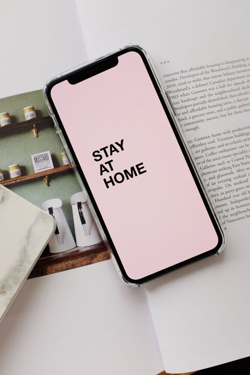 Free From above of modern mobile phone with pale pink screen and STAY AT HOME inscription placed on open magazine during coronavirus pandemic Stock Photo