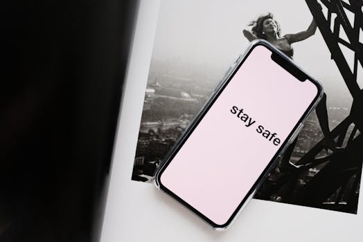 From above of cellphone pale pink screen with STAY SAFE inscription put on open magazine with photo of cheerful woman climbing metal tower in city